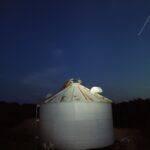 male and female peafowl atop a grain bin at night